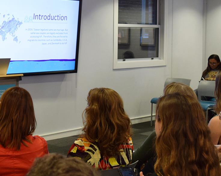 People seated listening to a speaker and looking at a presentation.